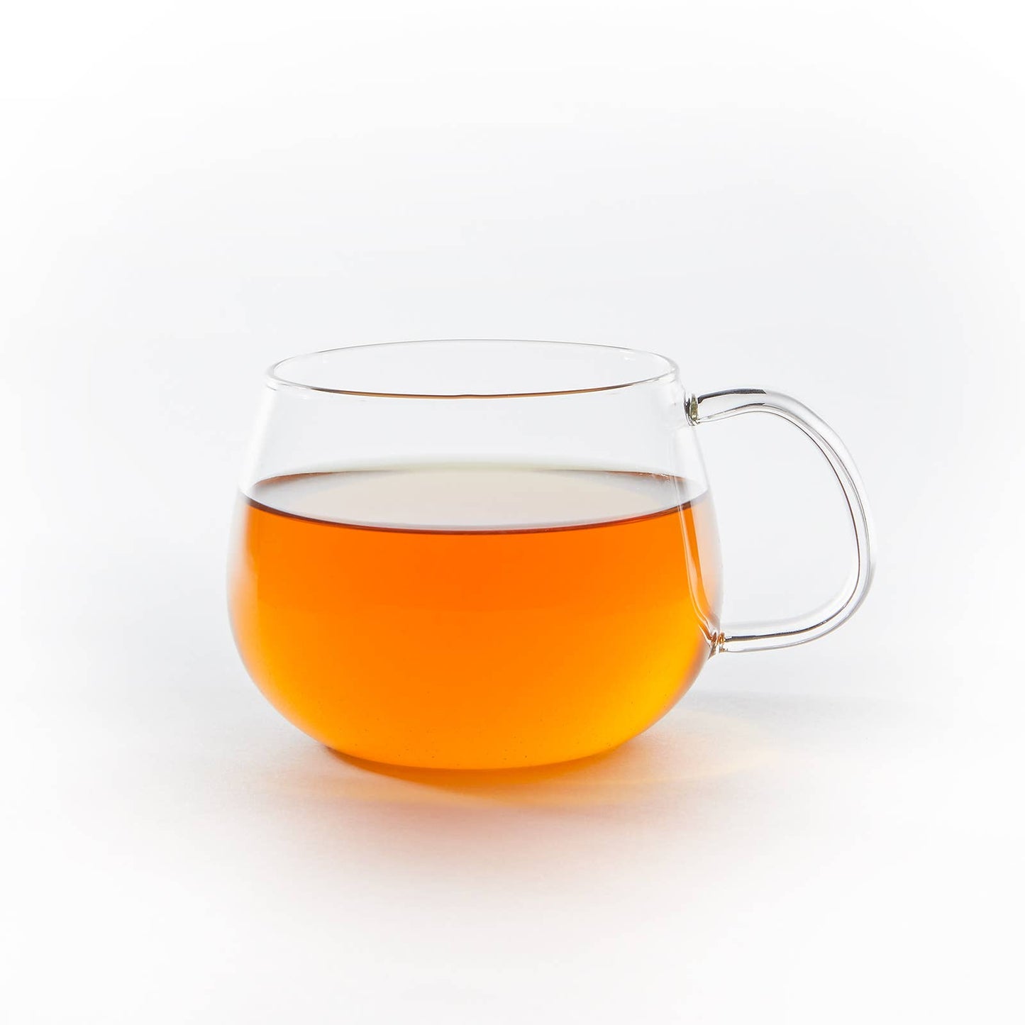 Clear glass mug with handle filled with orange liquid on a white background
