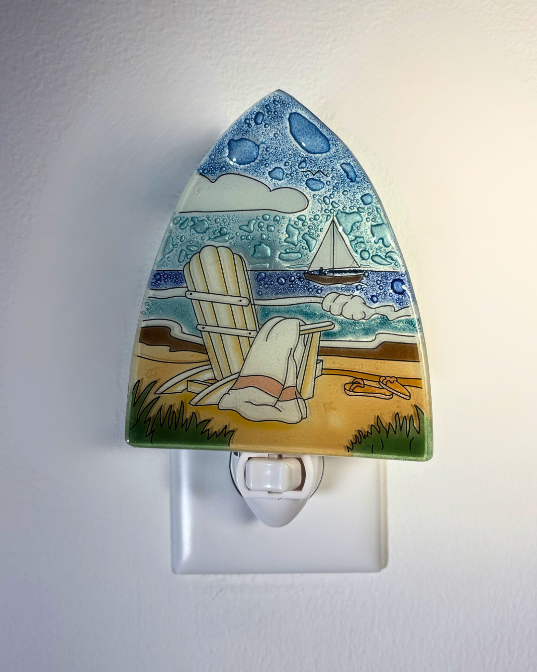Decorative night light with beach scene design on a white wall.