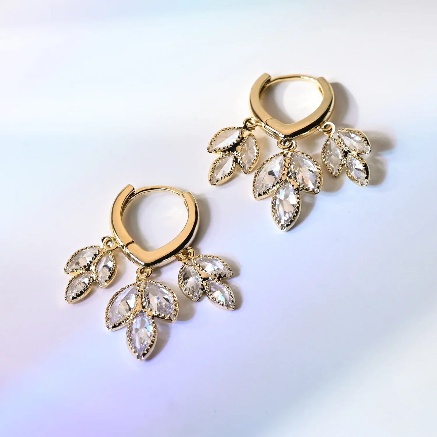 Gold hoop earrings with crystal-like stones on a light gradient background