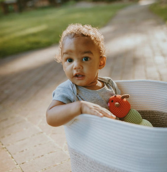 Child holding a red and green caterpillar toy in a basket outdoors