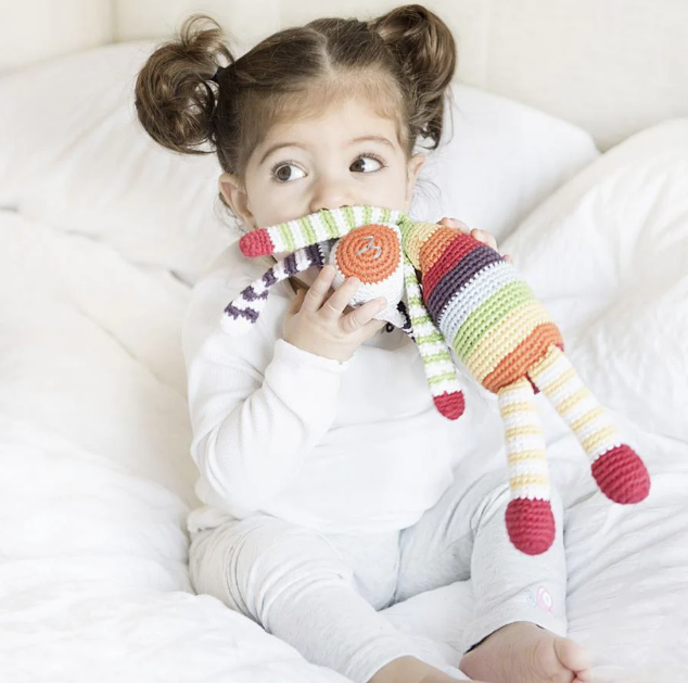A child with pigtails kisses a stuffed rainbow bunny.