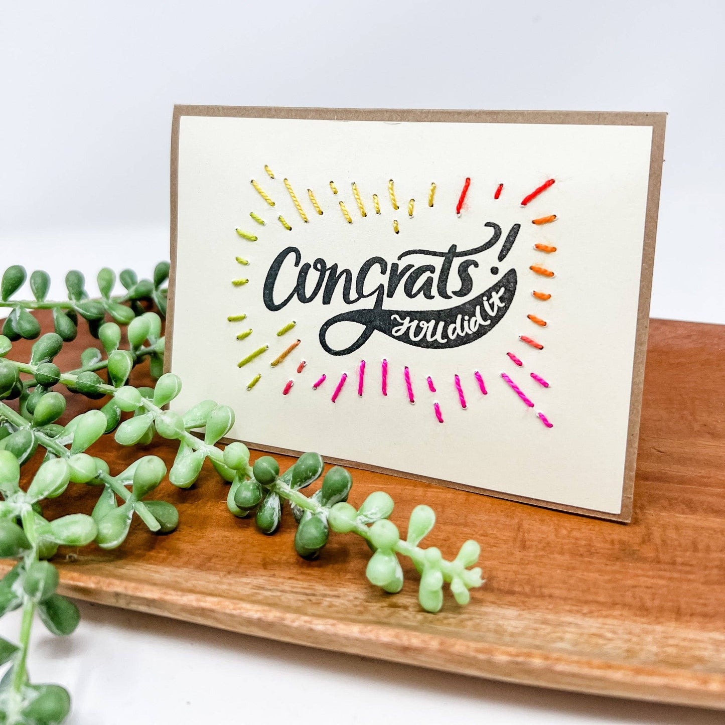 Greeting card with 'Congrats you did it!' text styled on a wooden surface with a plant.