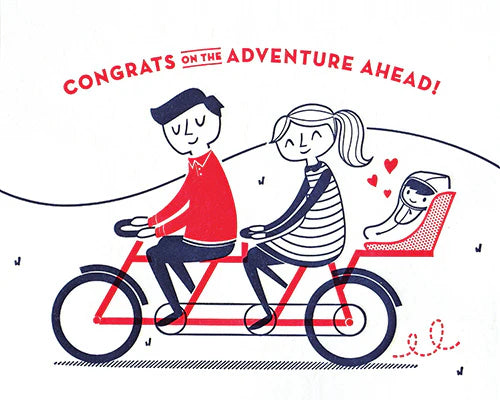 A greeting card with an illustration of a man and a woman riding a bicycle, with a baby in the back seat. The text on the card reads 'CONGRATS ON THE ADVENTURE AHEAD!'.