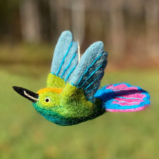 Colorful bird-shaped toy with green, blue, and pink feathers against a blurred natural background.