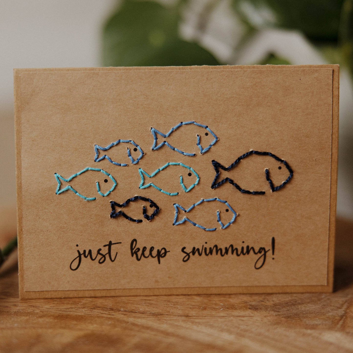 Card with embroidered fish and 'just keep swimming!' text on a brown recycled paper card.