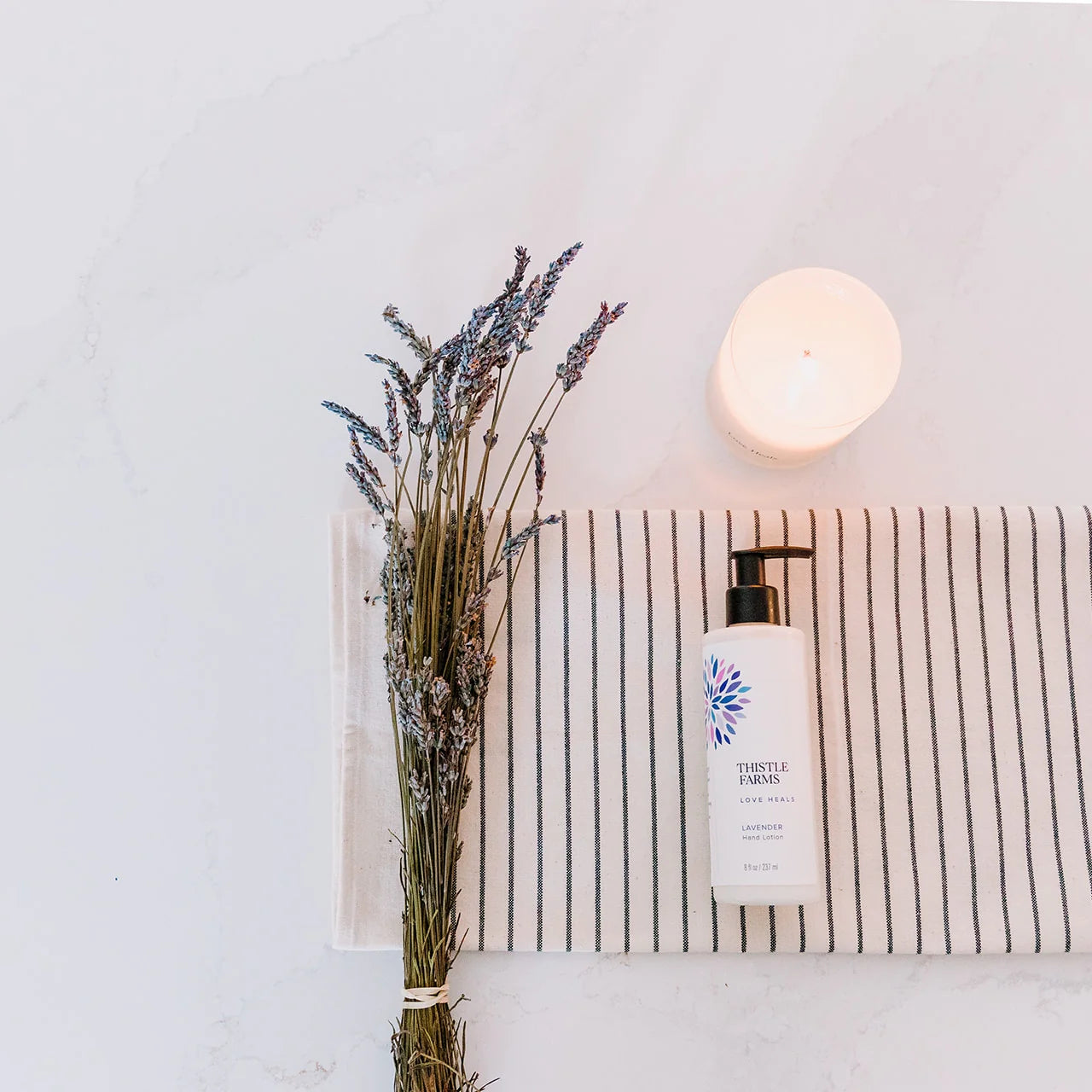 Lavender bottle on a striped towel with a candle in the background