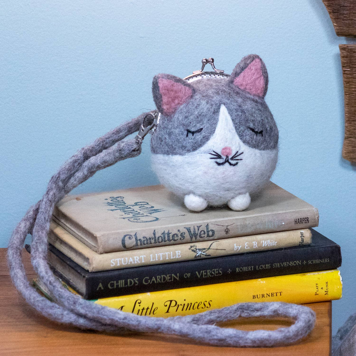 Cat-shaped felt purse with pink ears and white face on a stack of books