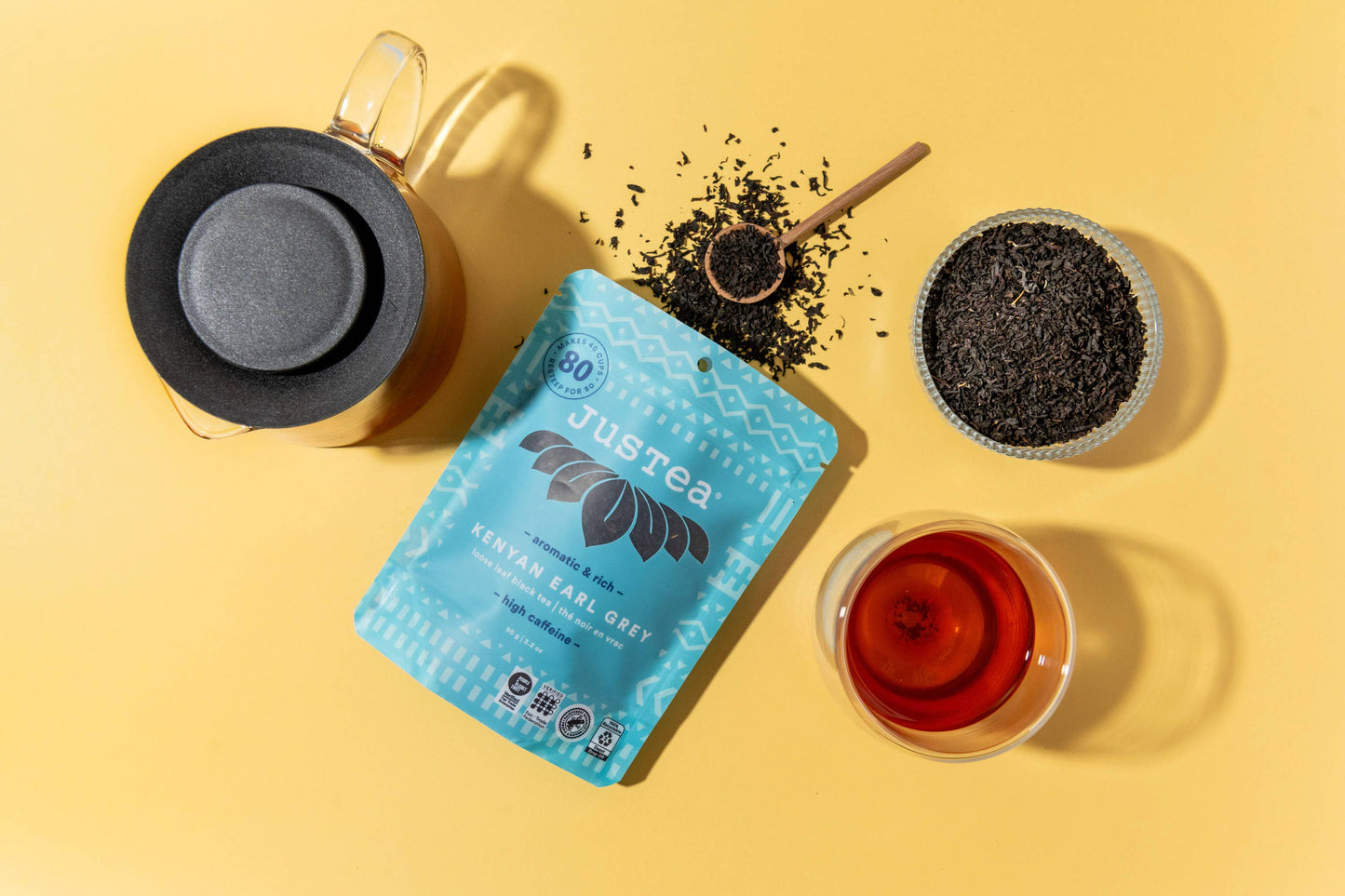 Jusrea tea packaging with a cup of tea, black tea leaves, and a spoon on a yellow background