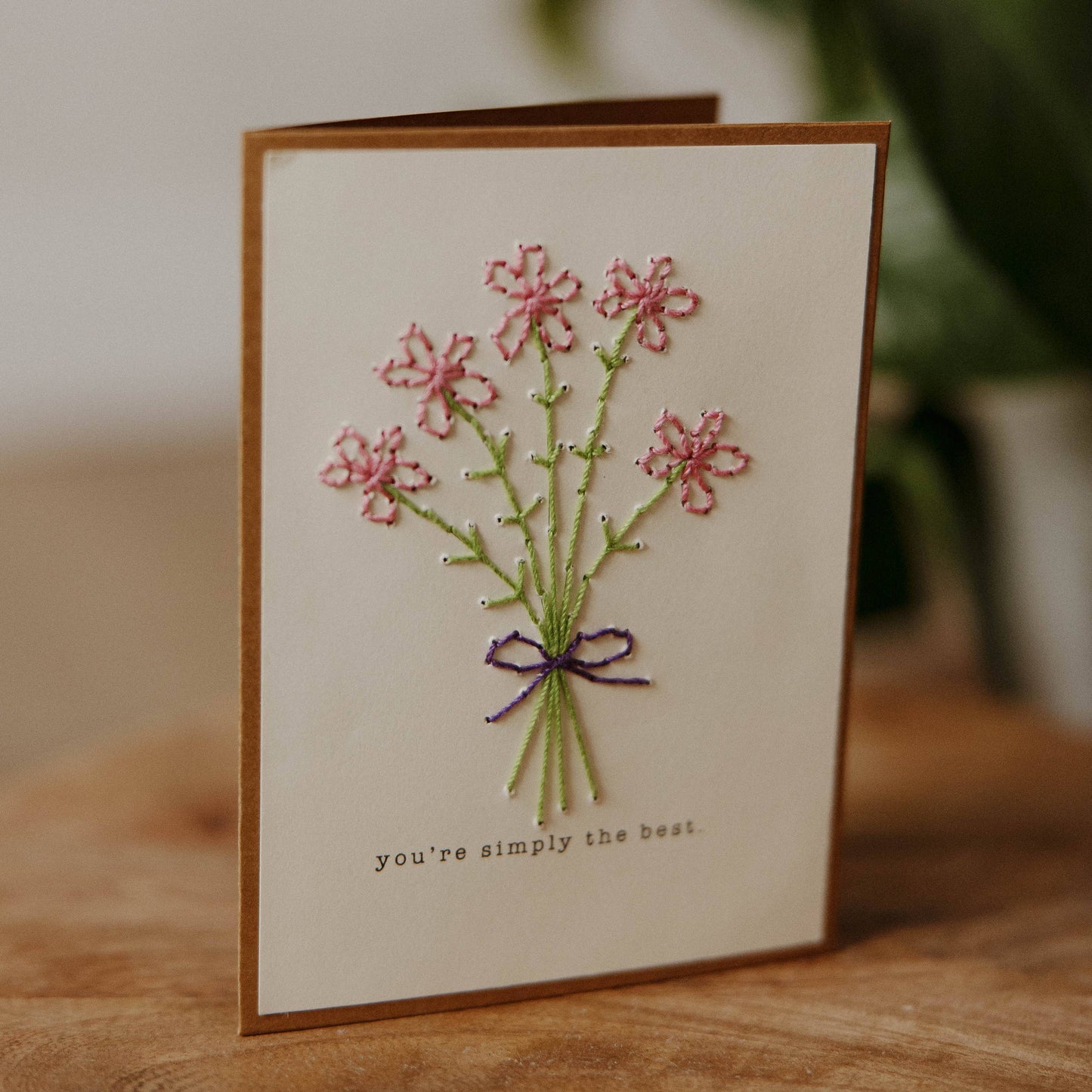 Greeting card with embroidered flowers and text on a wooden surface