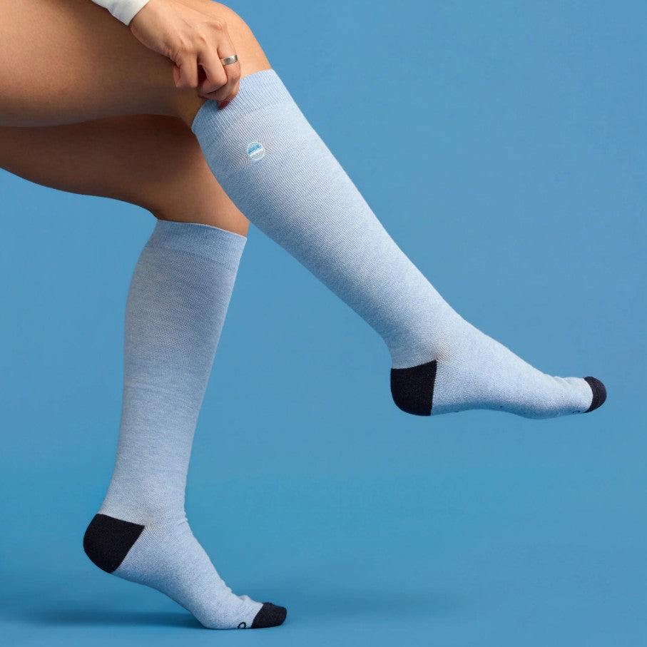 Light blue knee-high socks with navy toes and cuffs on a person against a blue background