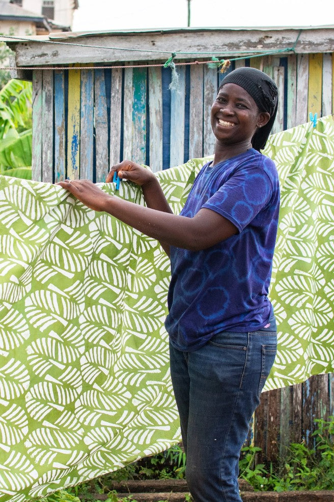 Person hanging green fabric with white leaf pattern on a clothesline.