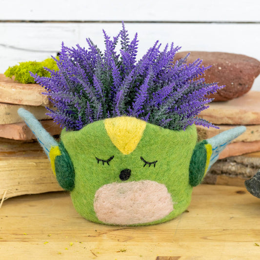 Green hummingbird pot with a face and purple flowers on a wooden surface