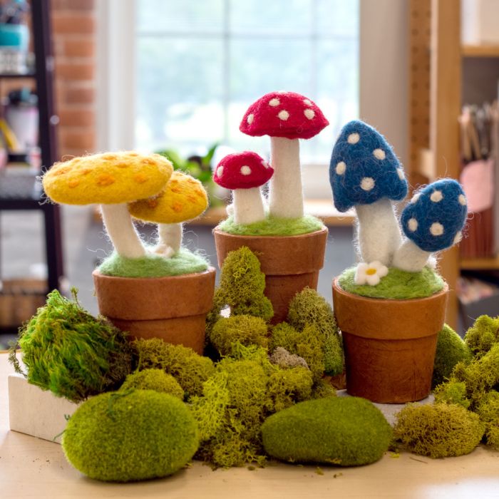 Colorful felt mushrooms in pots on a table with greenery.