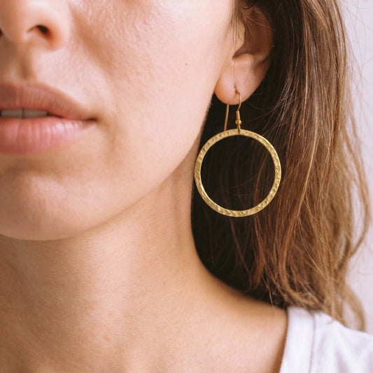 Close-up of a person wearing a gold circle hoop earring with a French hook.
