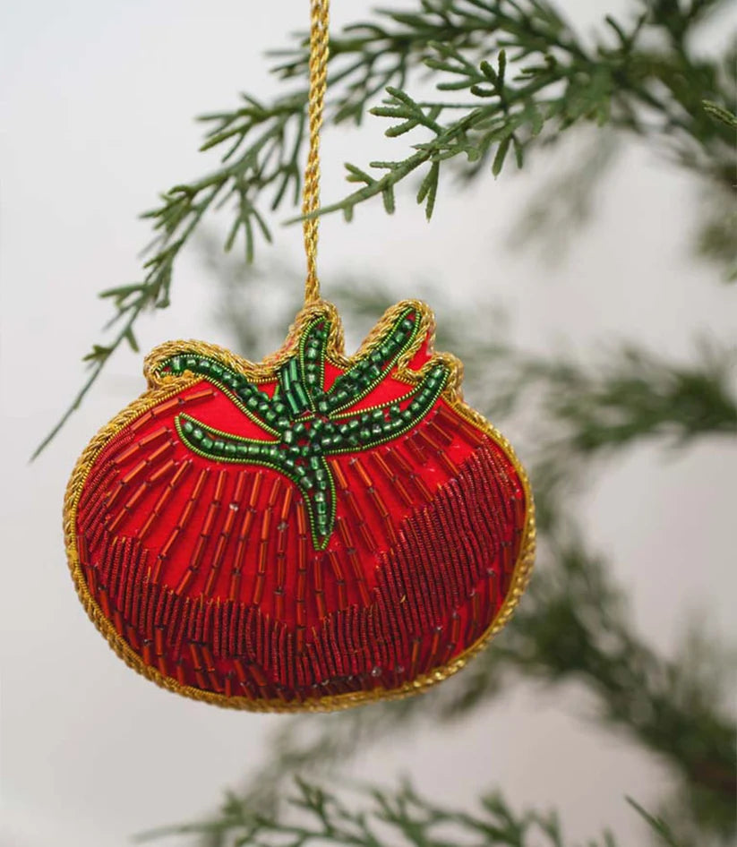 Close-up of a handcrafted tomato ornament featuring bright red beads, green embroidered leaves and a plush fabric base.