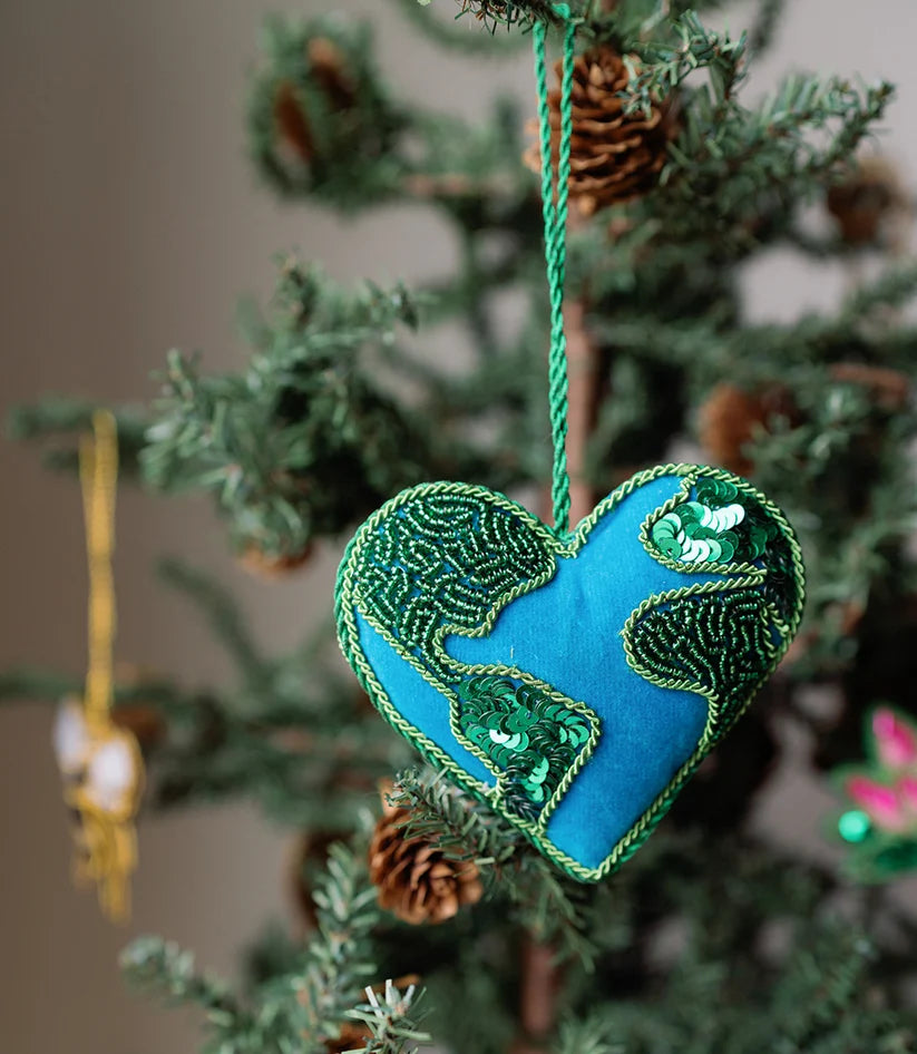 Close-up of a handcrafted heart-shaped Earth ornament showing intricate embroidery and colorful beaded continents.