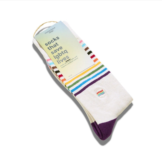 A pair of white socks with rainbow stripes and a purple toe, packaged with a paper tag that reads 'socks that save LGBTQ+ lives' on a white background.