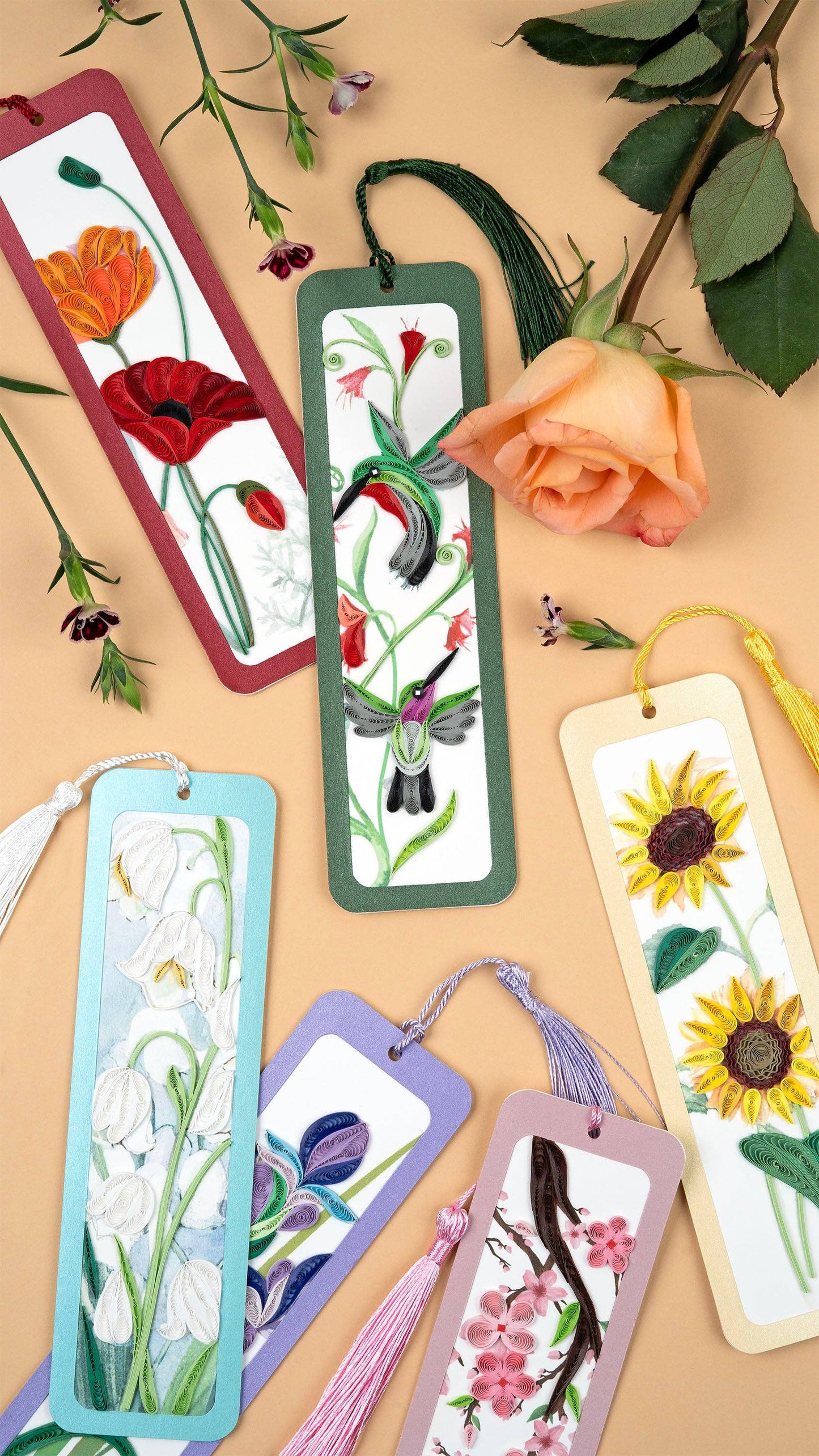 Six bookmarks in various colors and quilled patterns are arranged on a peach background and shown surrounded with flowers.