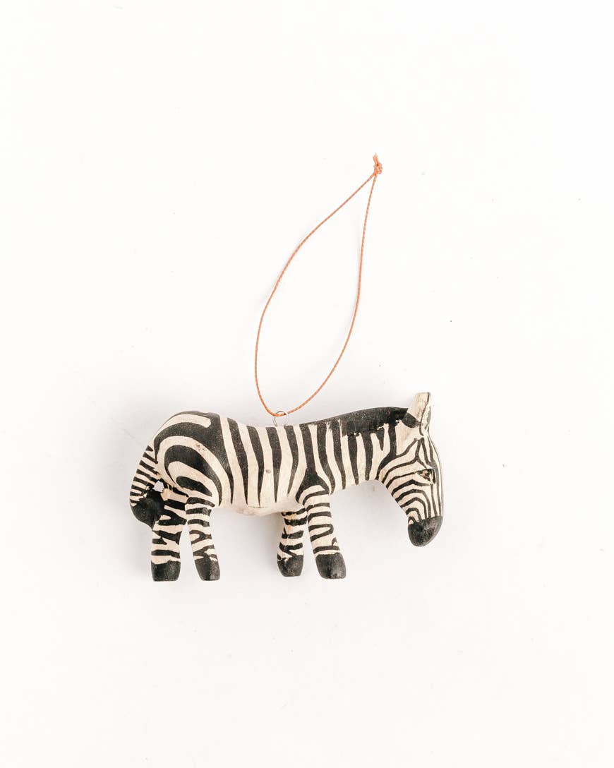 A small zebra-shaped hanging ornament with black and white stripes and a thin orange string, photographed on a plain white background.