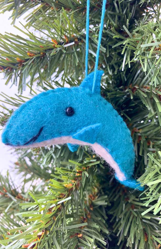 A blue felt dolphin ornament with a bead eye and stitch detail, hanging on a Christmas tree.