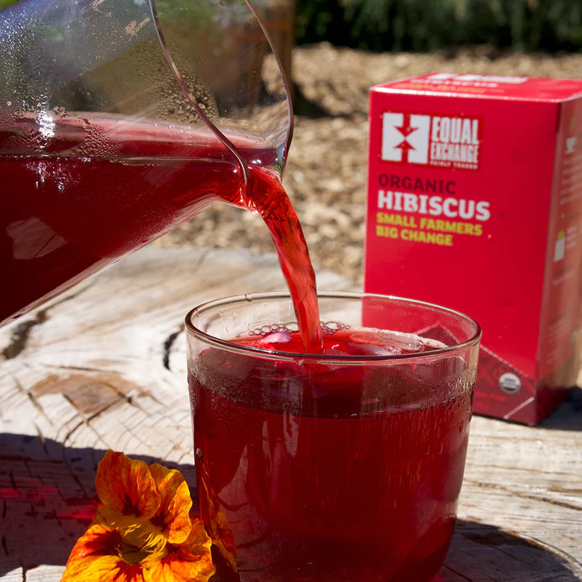 Red hibiscus tea being poured into a glass with an Equal Exchange Organic Hibiscus box in the background.