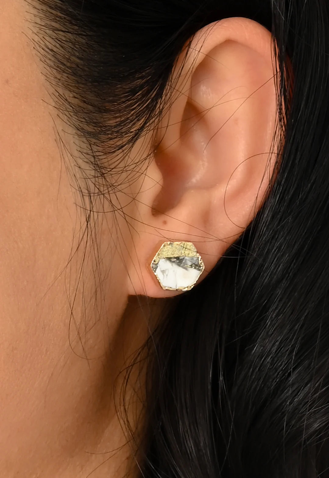 Close-up of an ear wearing a gold earring with a white textured stone.
