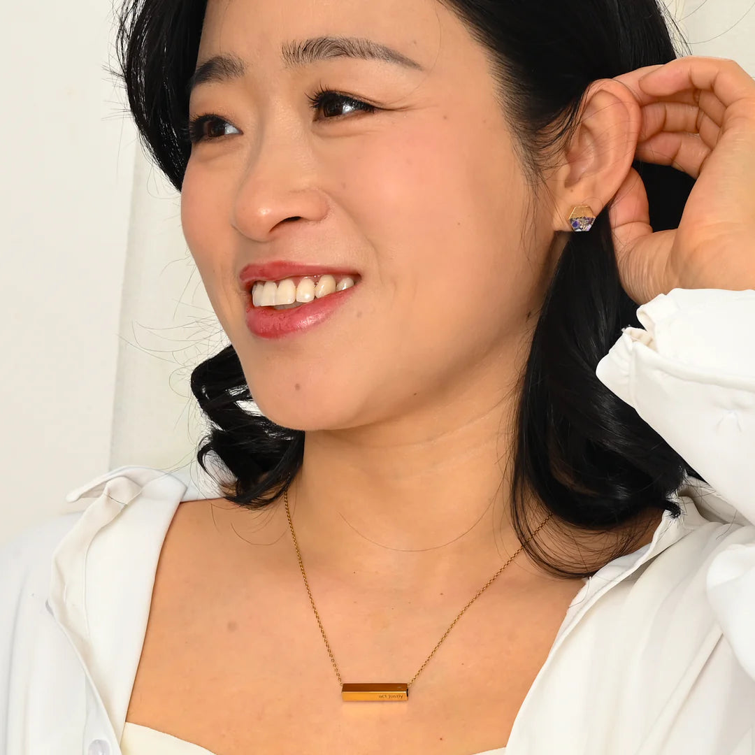 Model wearing hexagonal gold and purple stud earrings and rectangular pendant necklace.