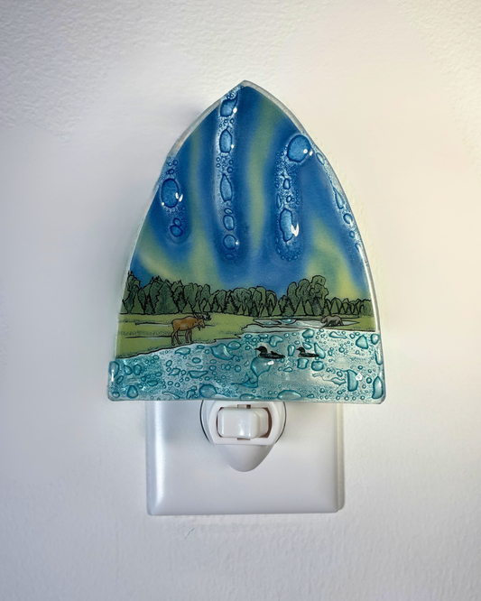 Decorative night light with a nature scene featuring a lake and animals on a white wall.
