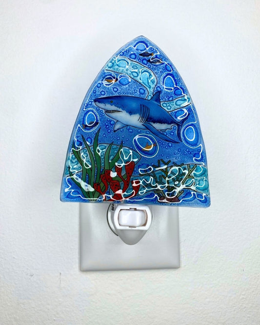 A decorative blue night light plug-in with a hand-painted shark and underwater scene, shown mounted on a white wall.