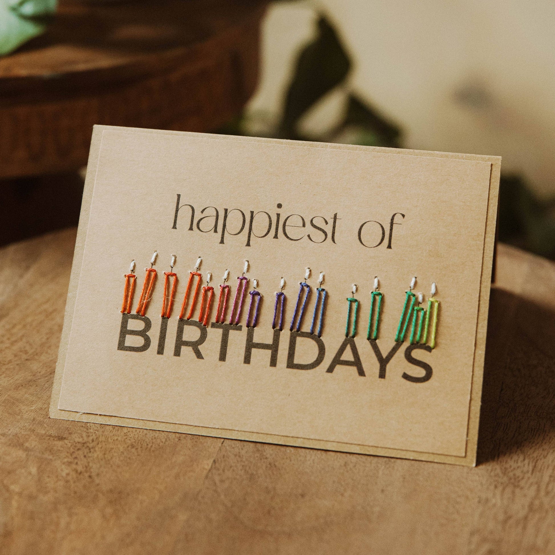 Greeting card with colorful candles and 'happiest of birthdays' text on a brown recycled paper card.