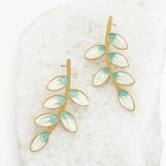 Gold and green leaf-shaped earrings on a textured white background
