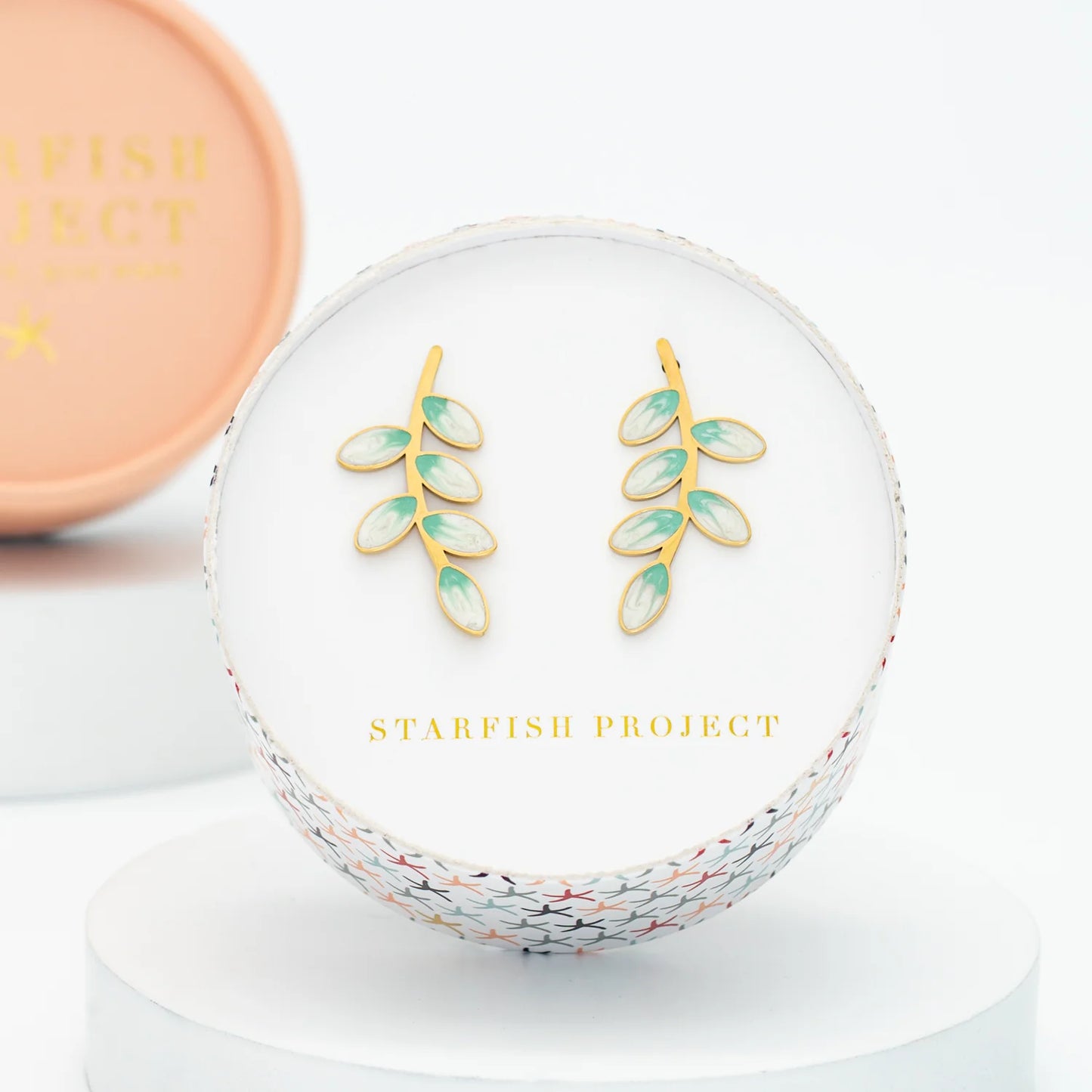 Gold and green leaf earrings inside a circular box with 'Starfish Project' branding.