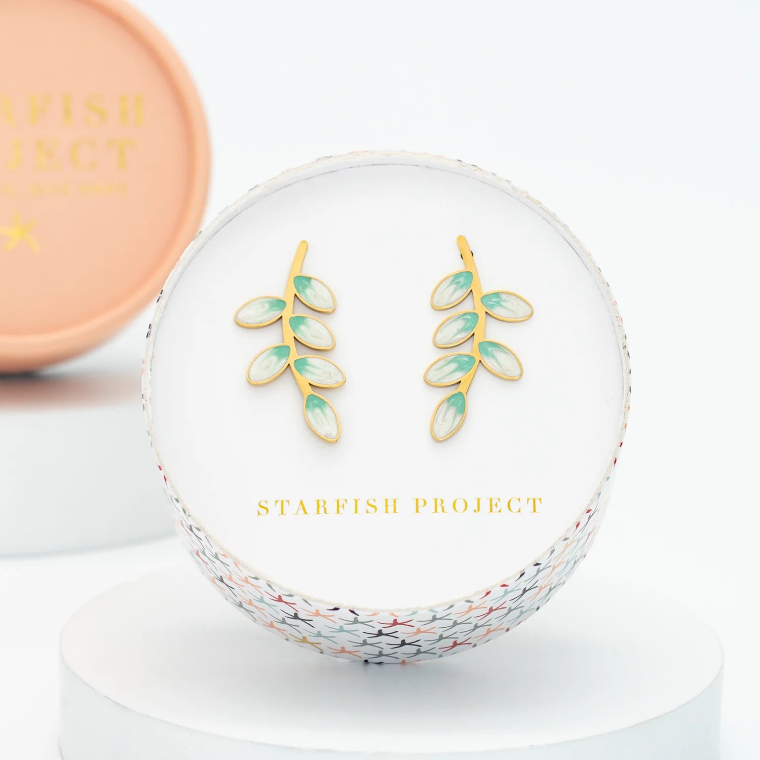 Gold and green leaf earrings inside a circular box with 'Starfish Project' branding.