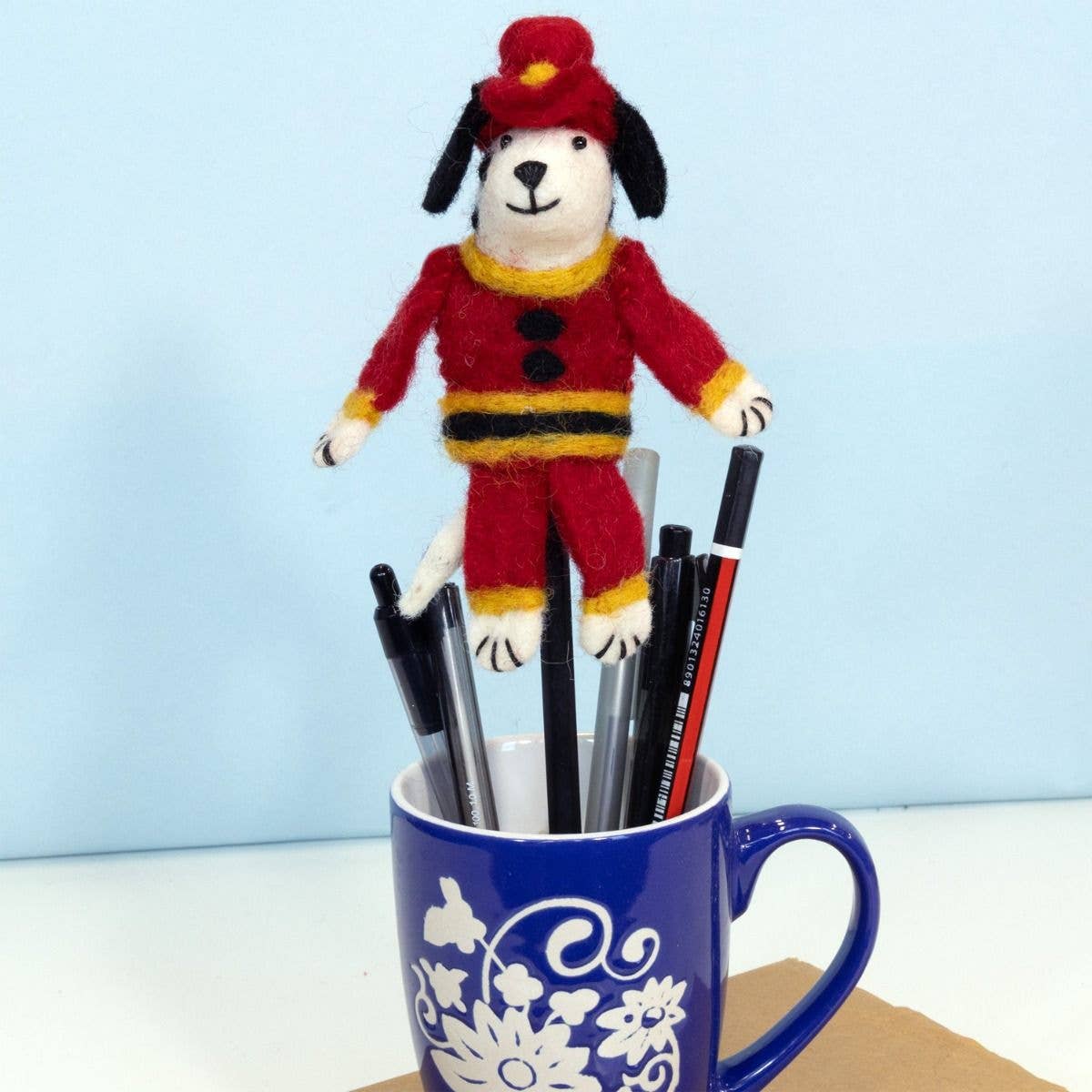 Dog-shaped ornament in a blue mug with pens on a light blue background