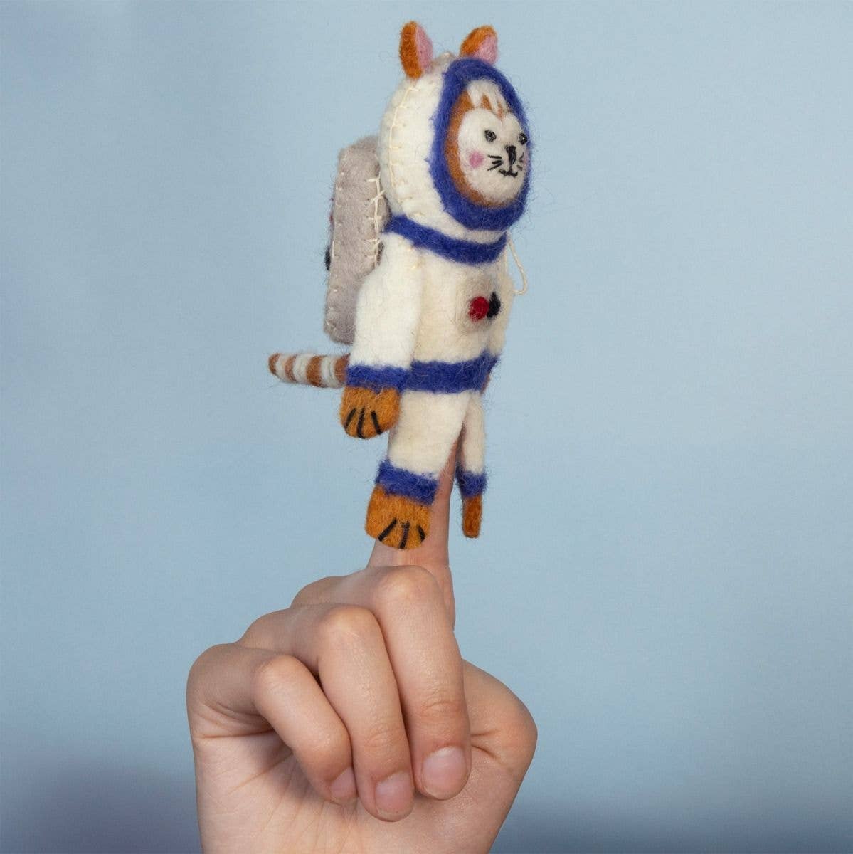 A hand holding a small felted wool astronaut cat figure against a soft light blue background.