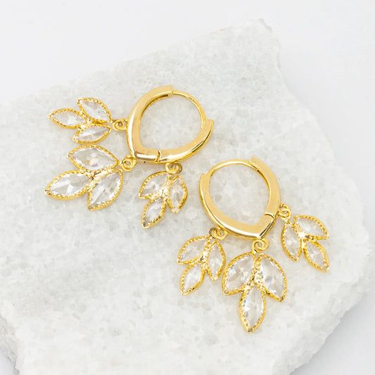 Gold hoop earrings with leaf-like sparkly drops on a white textured background