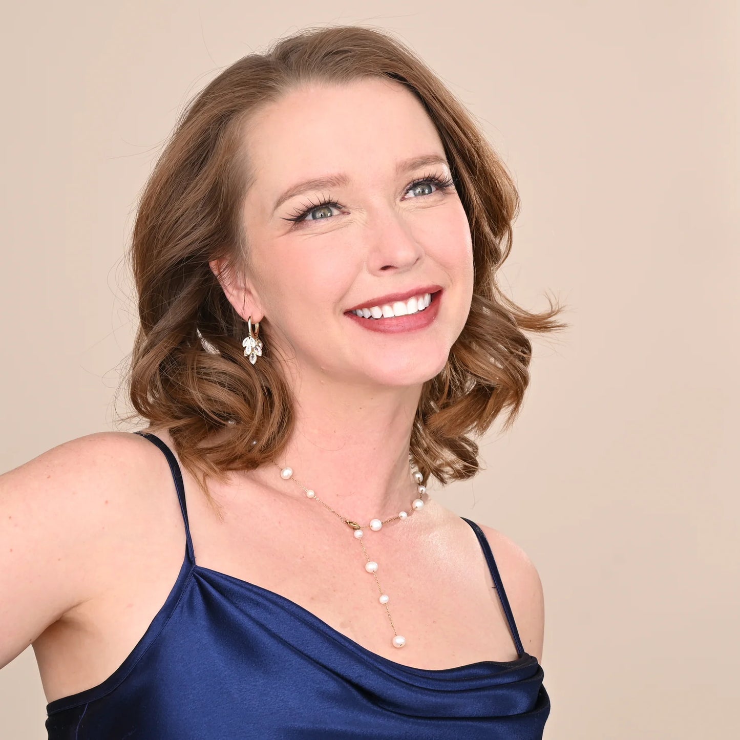 Woman wearing a blue dress with a pearl necklace and earrings against a beige background