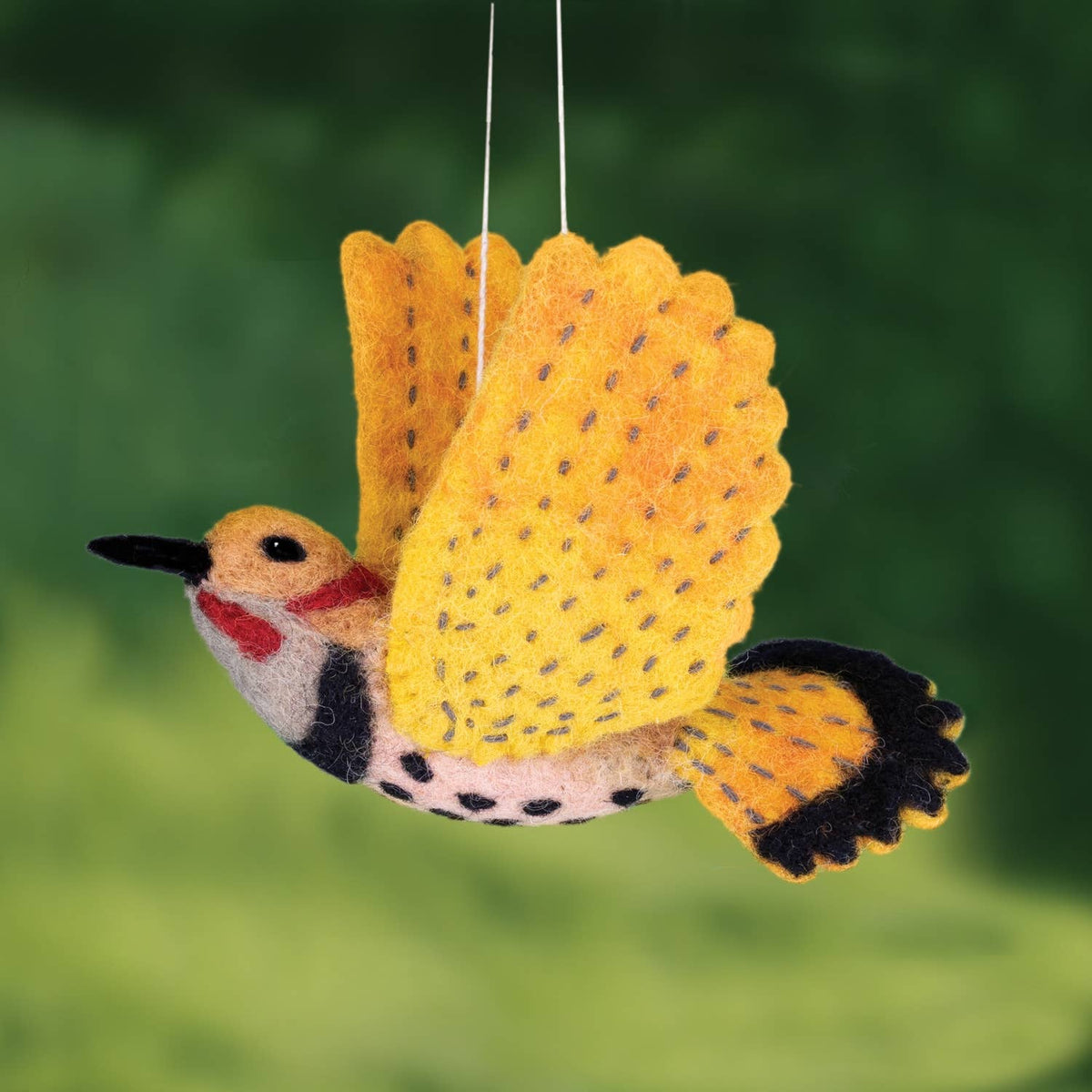 A felt bird ornament or decoration with bright yellow wings, black and white spotted body, red chest patch, and black tail, hanging against a blurred green background.