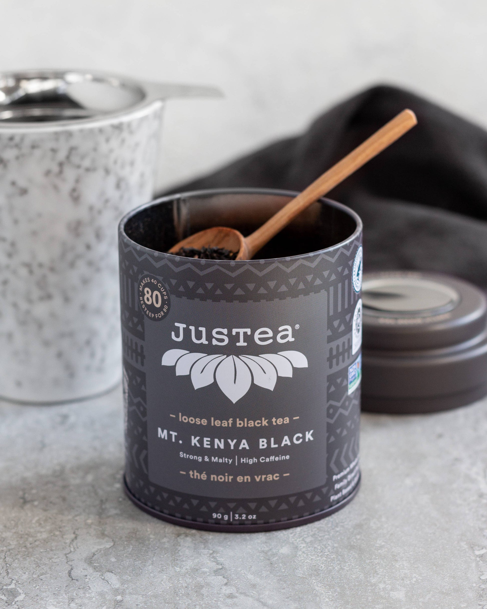 Justea Mt. Kenya Black tea canister with a wooden spoon on a light gray surface