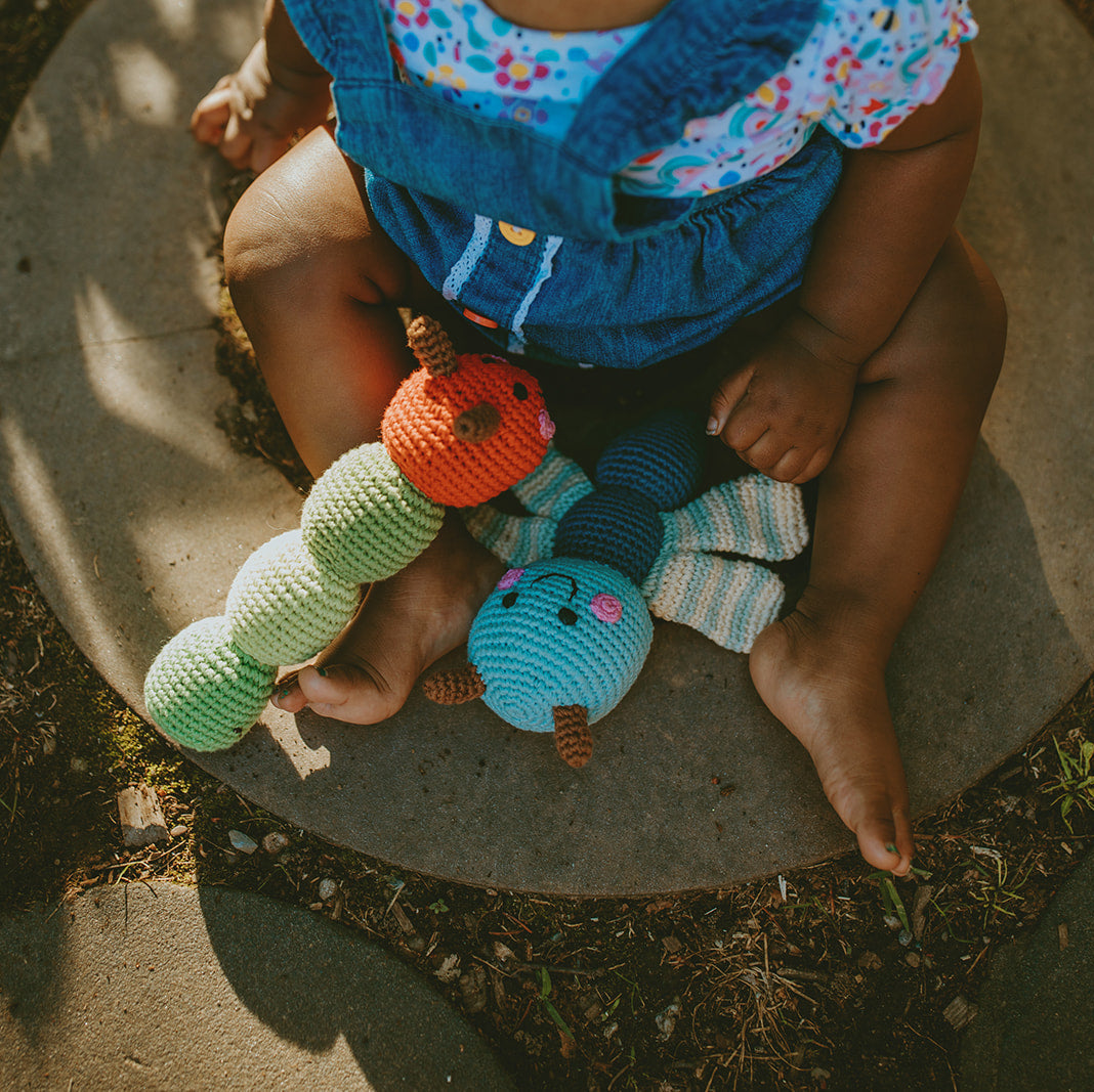Child sitting on a stone with colorful knit toys