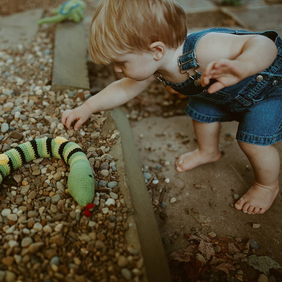 Child playing with a toy snake on a pebbled surface