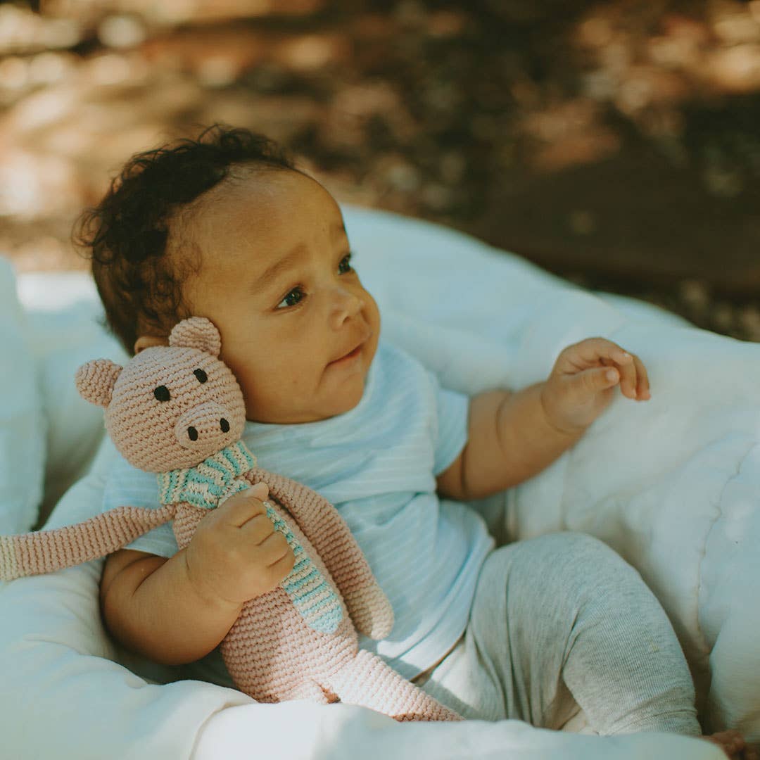 Baby holding a pink pig stuffed animal in an outdoor setting