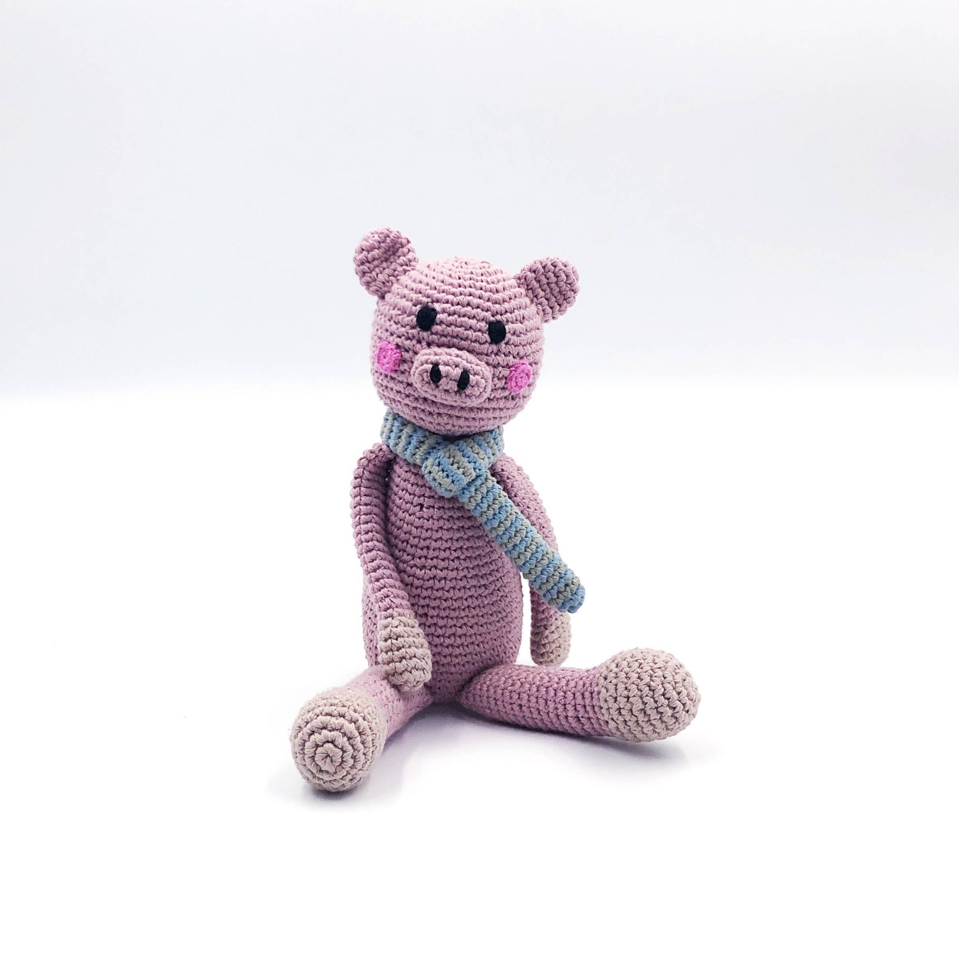 Crocheted pink pig toy with a blue scarf on a white background