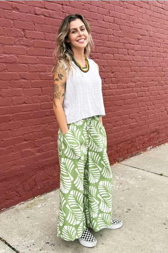Woman wearing green patterned pants and a white top against a red brick background.