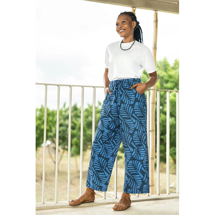 Woman wearing blue patterned pants and a white shirt on a balcony.