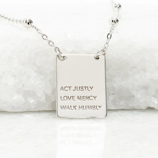 Square silver pendant with engraved message of "Act Justly. Love Mercy. Walk Humbly." on a white background