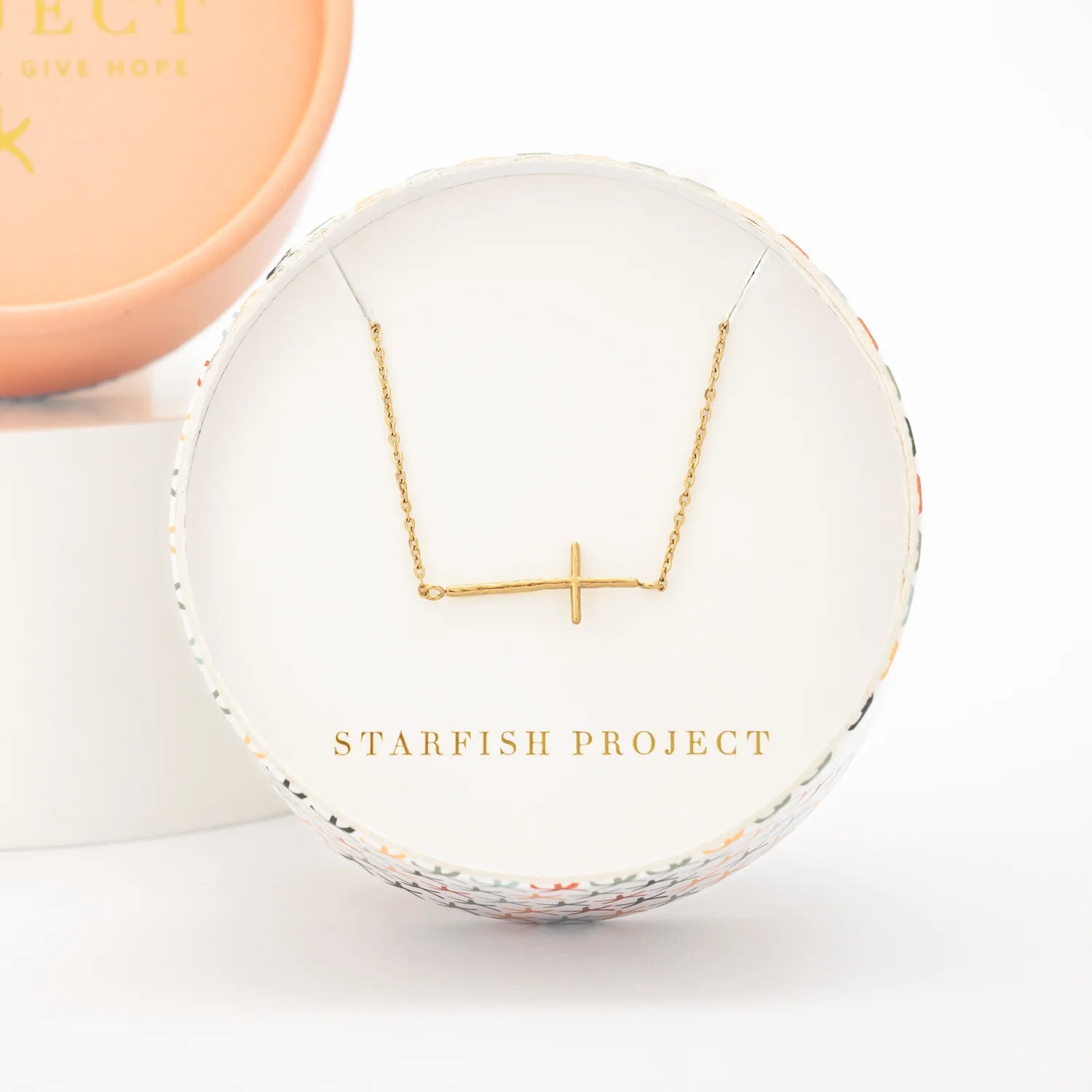 Gold horizontal cross necklace on a Starfish Project branded box with a white background