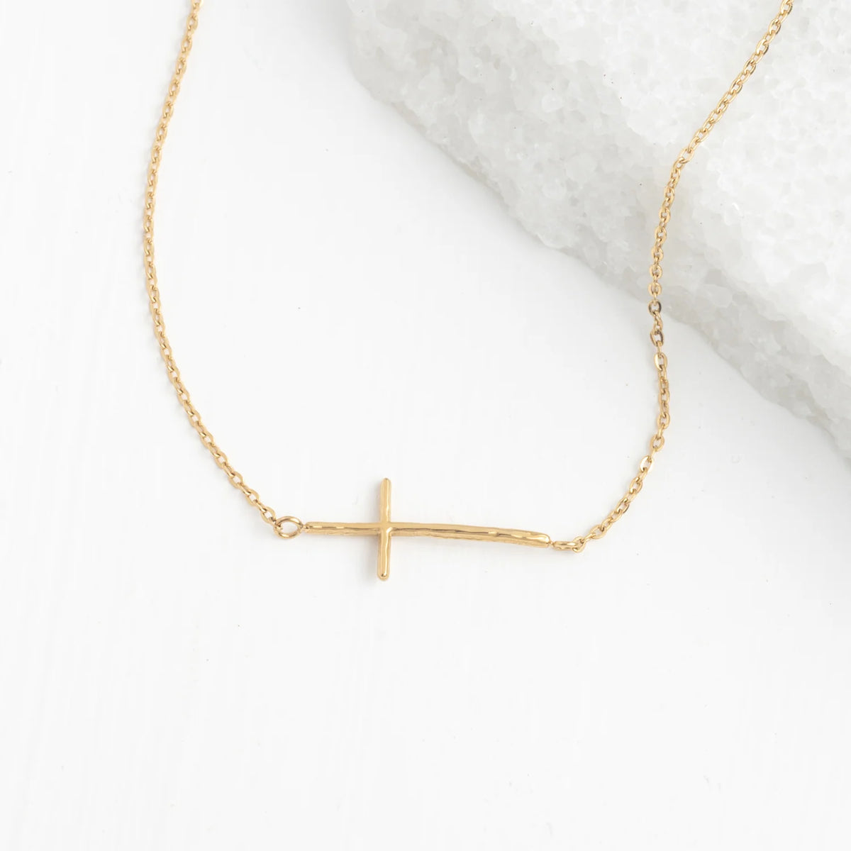 Gold necklace with a sideways cross pendant on a white background