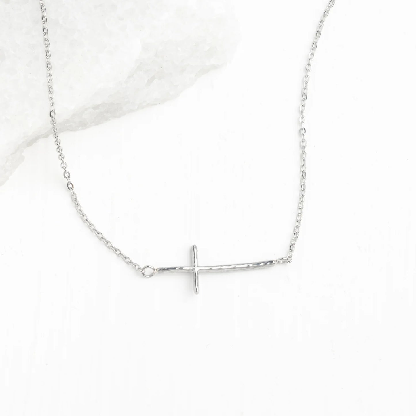 A delicate silver chain necklace featuring a horizontal cross pendant displayed on a light white background.