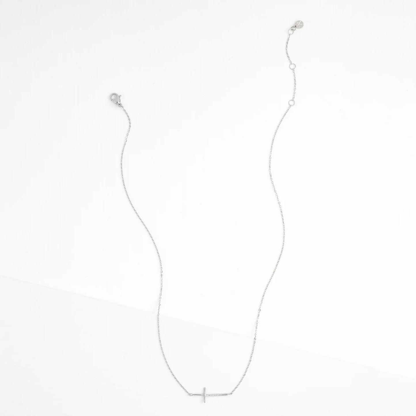 A delicate silver chain necklace with a small, minimalist cross pendant at the center, displayed against a clean white background.